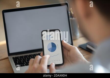 L'uomo d'affari sincronizza le informazioni utilizzando il laptop e lo smartphone con i dati finanziari Foto Stock