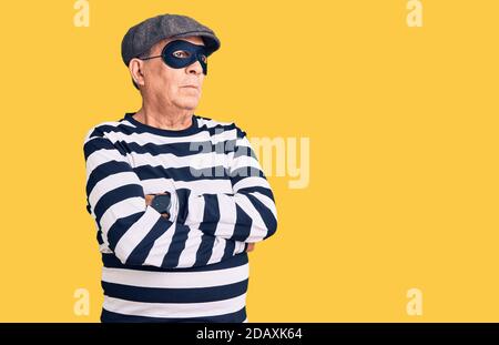 Uomo anziano bello che indossa maschera di scasso e t-shirt che guarda a. il fianco con le braccia incrociate convinto e fiducioso Foto Stock