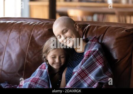 Madre che lotta con oncologia seduta sul divano abbracciando piccola figlia Foto Stock