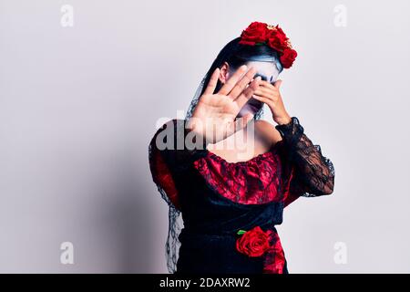 Giovane donna che indossa il giorno messicano del trucco morto coprendo gli occhi con le mani e facendo gesto di stop con espressione triste e paura. Imbarazzata e negata Foto Stock