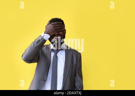 Il primo piano di un uomo afro americano dispiaciuto con la mano sulla testa soffiato in studio sfondo giallo Foto Stock