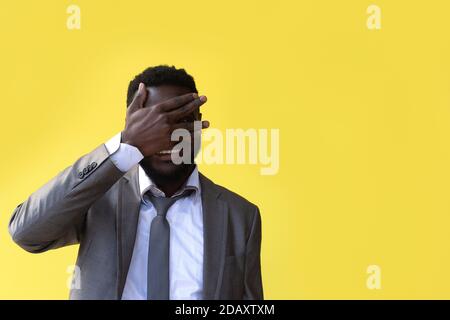 Il primo piano di un uomo afro americano dispiaciuto con la mano sulla testa soffiato in studio sfondo giallo Foto Stock