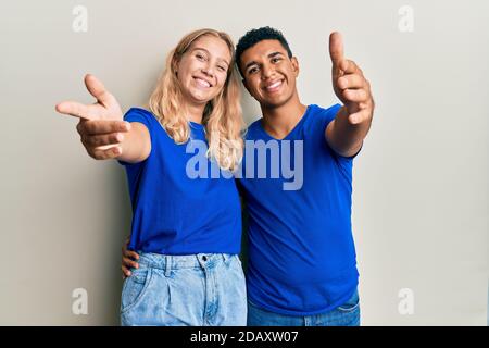 Giovane coppia interracial che indossa abiti casual sorridente amichevole offrendo handshake come saluto e accogliente. Business di successo. Foto Stock