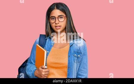 Giovane ragazza latina che indossa zaino studentesco e tiene libri che osservano sonnolento e stanco, esausto per stanchezza e sbornia, occhi pigri al mattino. Foto Stock