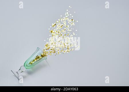 Un bicchiere verde versato con glitter dorato su sfondo bianco Foto Stock