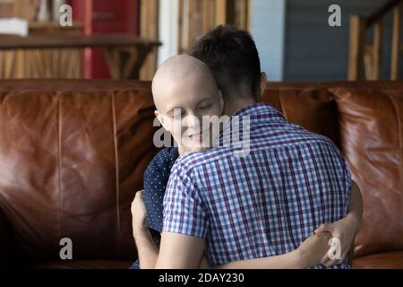 Coppia amorevole dove la donna è paziente di cancro abbracciando sul divano Foto Stock