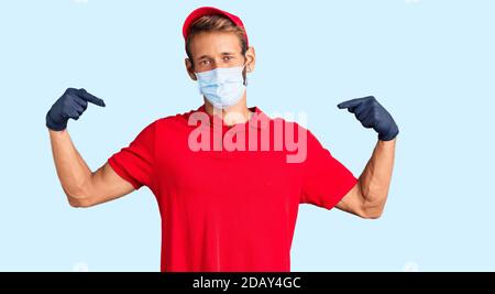 Bell'uomo biondo con barba che indossa uniforme e maschera medica che guarda sicuro con sorriso sul viso, puntandosi con le dita orgogliose e Foto Stock