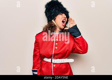 Di mezza età bella donna guardia gallese indossare uniforme tradizionale su sfondo bianco gridare e gridare forte a fianco con la mano sulla bocca. Commu Foto Stock