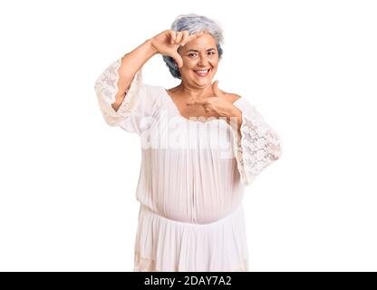 Donna anziana con capelli grigi in stile bohémien sorridente che fa cornice con mani e dita con volto felice. Creatività e concetto di fotografia. Foto Stock