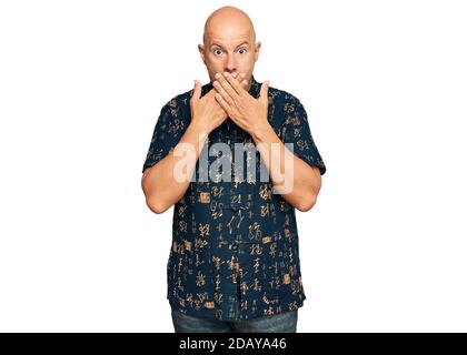 Uomo calvo di media età che indossa abiti casual scioccato coprendo la bocca con le mani per errore. Concetto segreto. Foto Stock