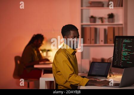 Ritratto dello sviluppatore IT afro-americano che scrive codice su più schermi di computer mentre lavora in ufficio, copia spazio Foto Stock