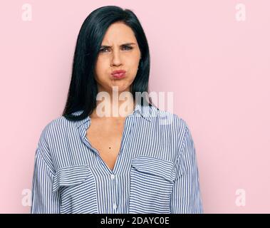 Giovane donna caucasica che indossa abiti casual soffia guance con viso divertente. Bocca gonfia con aria, espressione pazza. Foto Stock