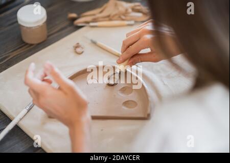 Primo piano di un attrezzo speciale per il taglio dell'argilla e del vasaio principale. Taglio di artista femminile con un utensile ad anello in legno Foto Stock