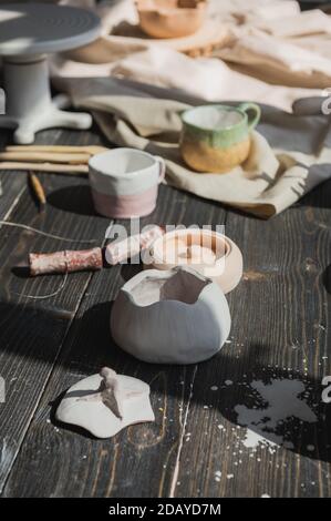 Una vista ravvicinata di piatti in argilla e un pennello su un tavolo di legno e fiori secchi su uno sfondo. Stoviglie artigianali in uno studio di ceramica. Fatto a mano Foto Stock