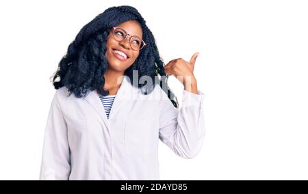 Bella donna opticista afroamericana con occhiali da ottometria sorridente con faccia felice guardando e puntando al lato con il pollice in su. Foto Stock