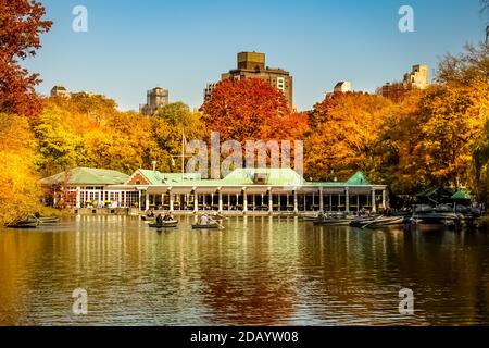 La Loeb Boathouse in Central Park in una giornata di sole autunno con le persone che girovagano in barche con alberi gialli e rossi che cambiano colore. Foto Stock