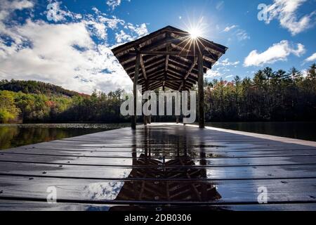 Sunburst sopra il molo di legno sul lago Dense - Foresta ricreativa di Stato di DuPont - vicino a Cedar Mountain, Carolina del Nord, Stati Uniti Foto Stock
