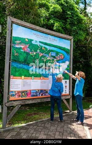 Due visitatori che guardano una grande mappa delle cascate e dei sentieri per i piedi nel Parco Nazionale di Iguazu dell'Argentina. Foto Stock