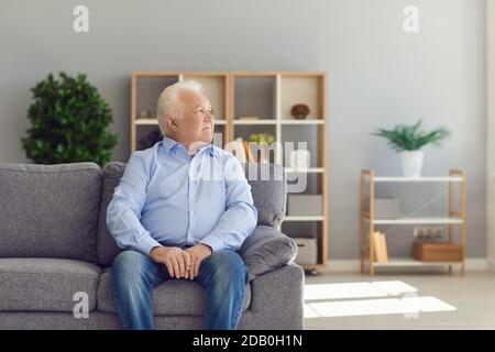 Uomo anziano seduto sul divano in soggiorno pensando a vita e ricordi del passato Foto Stock