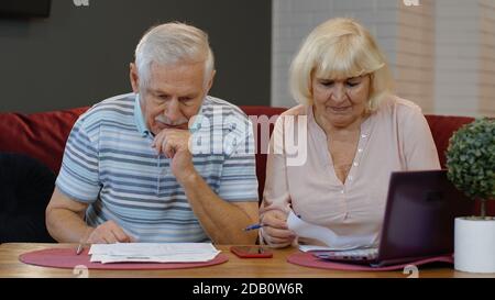 Preoccupato anziano anziano che controlla le fatture che calcolano il pagamento del prestito bancario che fa il lavoro di ufficio discutono le tasse di debito non pagate, ha sottolineato la famiglia dei nonni vecchi sguardo al laptop sconvolto circa il concetto di problema di soldi Foto Stock