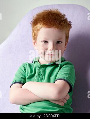 Carino ragazzino rosso dai capelli reckled in t-shirt verde in attesa per medico in ufficio medico Foto Stock