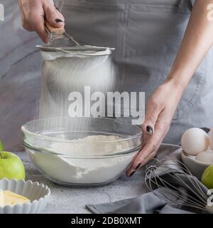 Donna setacciando la farina attraverso il setaccio, preparando torta dolce fatta in casa con mele mature Foto Stock