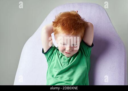 Carino ragazzino rosso dai capelli reckled in t-shirt verde in attesa per medico in ufficio medico Foto Stock