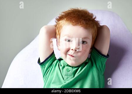 Carino ragazzino rosso dai capelli reckled in t-shirt verde in attesa per medico in ufficio medico Foto Stock