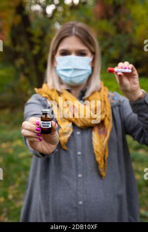 Donna caucasica con maschera sta tenendo covid test tube e. vaccino all'aperto durante la pandemia globale Foto Stock