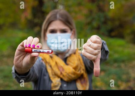 Giovane donna caucasica con maschera sta tenendo una provetta con il campione di sangue, che ha covid-19 sintomi Foto Stock