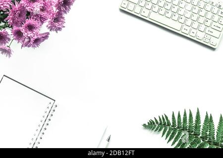 Taccuino, penna, tastiera, bouquet di crisantemi rosa e foglie di felce su sfondo bianco. Ambiente di lavoro accogliente, vista dall'alto, spazio per fotocopie. Foto Stock