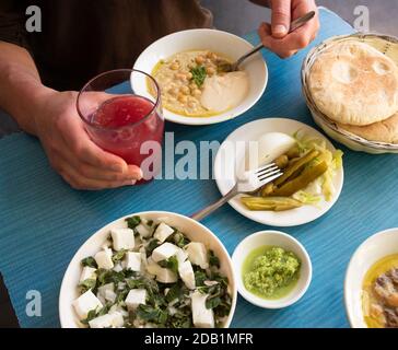 Uomo che mangia hummus caldo fresco con pane pita, sottaceti, insalata di formaggio feta con erbe biologiche e bere succo di frutta fresco spremuto. Mangiare sano. Foto Stock