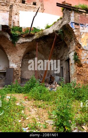 Casa abbandonata in rovina vicino a un edificio residenziale. Muro di pietra rotto e archi sostenuti da arbusti di metallo. Ridurre i concetti di pericolo. Foto Stock