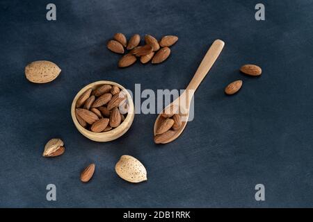 Mandorle in una ciotola di legno e su un cucchiaio di legno su un tavolo di legno nero. Vista dall'alto Foto Stock