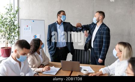 Due uomini d'affari in maschere che saltano i gomiti durante il Corporate Meeting Indoor Foto Stock