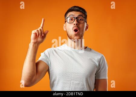 Nerdy ha sorpreso l'uomo in occhiali che ha un'idea mettere il dito verso l'alto Foto Stock