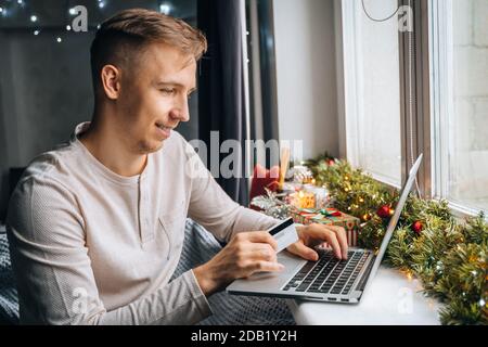 uomo cliente che detiene carta di credito shopping online effettuare il pagamento in negozio internet a casa. Decorazione scatola regalo di Natale, vendita inverno di Capodanno, Natale d Foto Stock