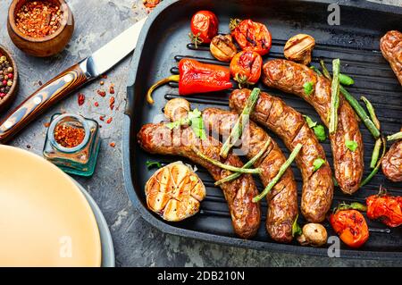 Salsiccia alla griglia con funghi e pomodori in padella Foto Stock