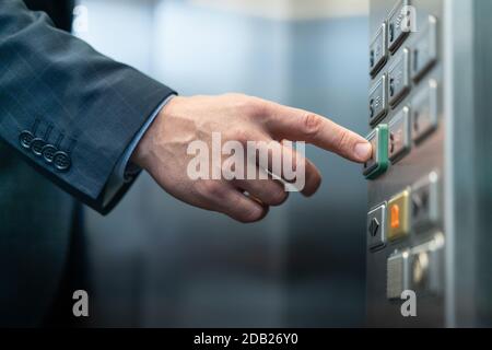 Uomo d'affari preme il pulsante con il braille per ciechi. Primo piano della mano maschio caucasica premendo il tasto per chiudere le porte nell'ascensore del business center Foto Stock