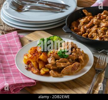 carne di maiale saltata con salsa alla crema, patate fritte e verdure su un piatto con padella Foto Stock