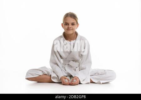 Ragazza sportiva in keikogi si siede sul pavimento, sfondo bianco Foto Stock