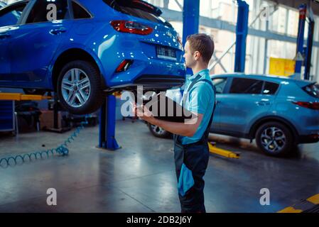 Riparatore con una lista di controllo si trova sul veicolo, sulla stazione di servizio auto. Controllo e ispezione di automobili, diagnostica professionale e riparazione Foto Stock