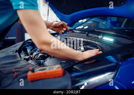 L'elettricista automatico in uniforme controlla i circuiti elettrici sulla stazione di servizio dell'automobile. Controllo e ispezione di automobili, diagnostica professionale e riparazione Foto Stock