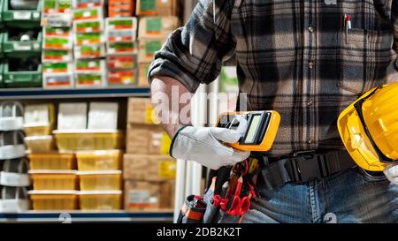 L'elettricista tiene a portata di mano il tester per multimetro, l'elmetto con occhiali di protezione. Industria edile, impianto elettrico. Foto Stock