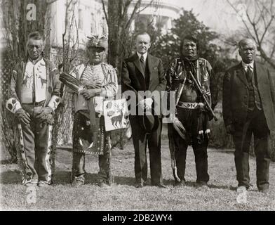 Il presidente Calvin Coolidge pose un ritratto a tutta lunghezza, in piedi, di fronte, con quattro indiani Osage; Casa Bianca sullo sfondo. Foto Stock