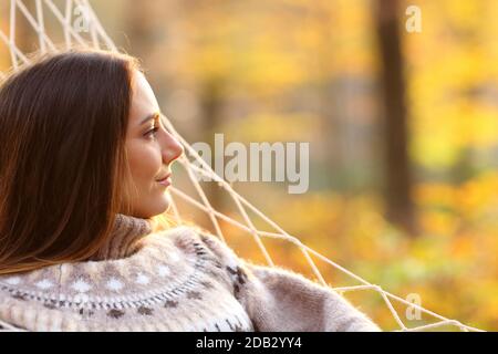 Vista laterale ritratto di una donna rilassata che contempla viste amaca in una foresta in autunno al tramonto