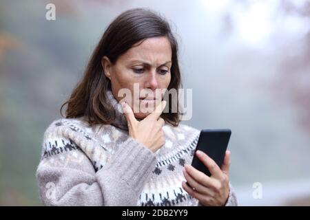 Donna di mezza età preoccupata che legge il messaggio dello smartphone in autunno stagione Foto Stock