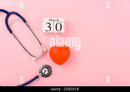 Concetto del giorno del medico, vista dall'alto a disposizione piatta, cuore rosso medico dell'apparecchiatura e stetoscopio su sfondo rosa, paziente di cura in ospedale con lo spazio della copia per Foto Stock