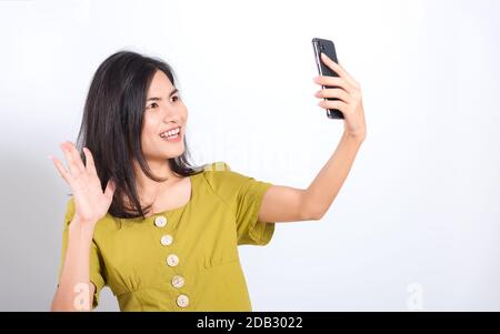 Ritratto asiatico bello felice giovane donna in piedi sorriso, tenendo cellulare suo prendere selfie su sfondo bianco, con spazio copia Foto Stock