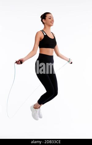 Spotrswoman salta con corda su sfondo bianco isolato. Fitness femminile facendo esercizio fisico. Concetto di salute e peso Foto Stock